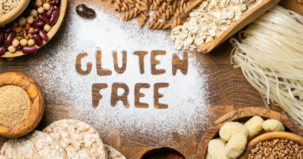 Palavras “GLUTEN FREE” escritas em farinha, cercadas por grãos, massas e alimentos em uma mesa de madeira
