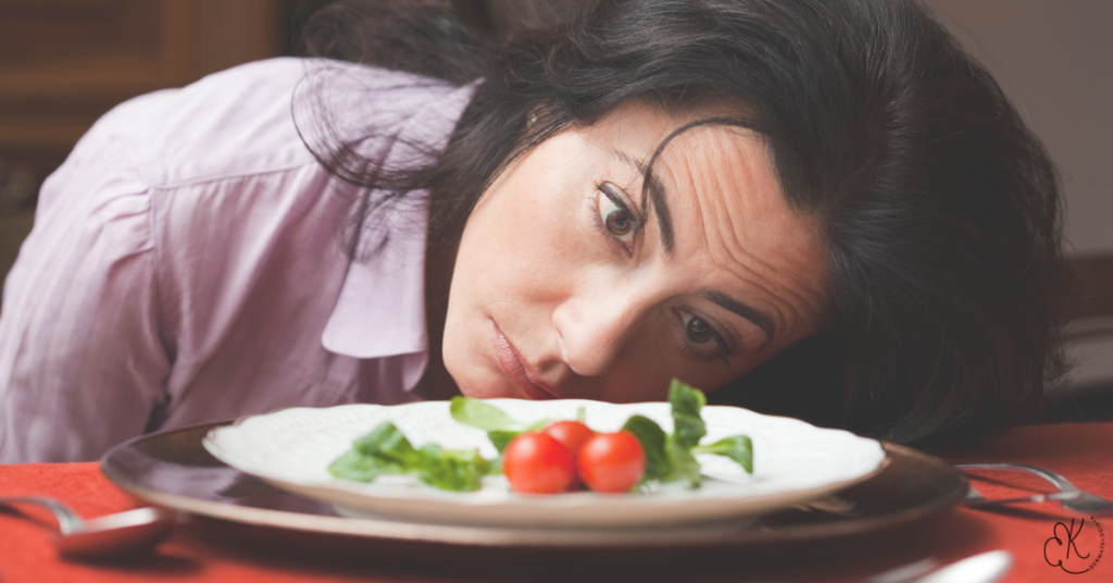 Mulher deitada sobre a mesa olhando para um prato com dois tomates cereja e folhas verdes