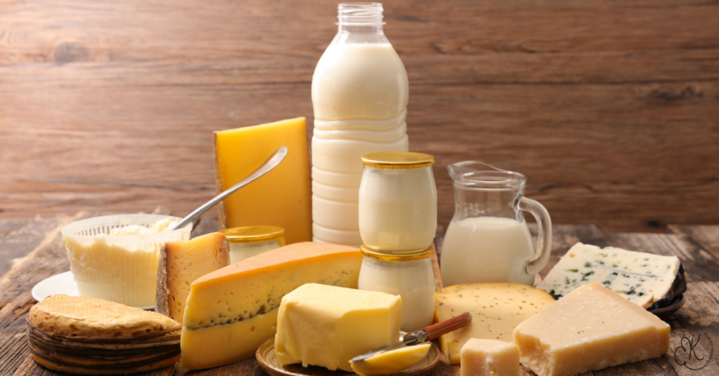 Variedade de alimentos lácteos como leite, queijos, iogurte e manteiga dispostos sobre mesa de madeira